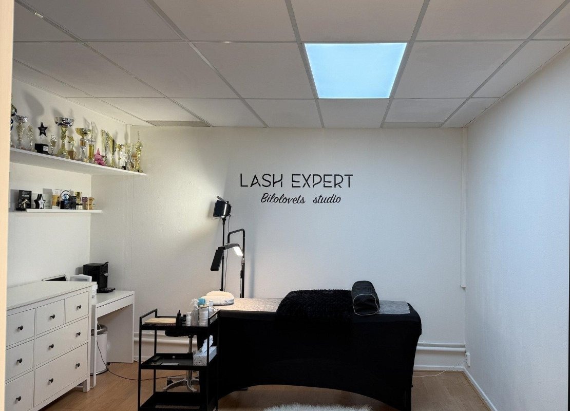 De behandelkamer van Lash expert Bilolovets studio: een zwarte behandelbank onder de letters LASH EXPERT Bilolovets studio op de witte muur